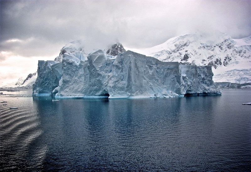 Immense iceberg devant les falaises enneigées - Antarctique | Les Mondes Polaires